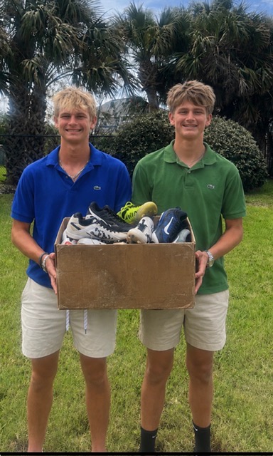 Founders holding a box full of donated cleats from the summer cleat drive